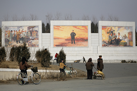 Koreans walk past massive propaganda mosaics of Kim Jong Il and Kim Il Sung on the outskirts of Pyongyang, North Korea
